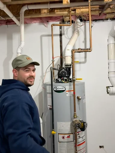Friendly Elevate Plumbing technician standing next to a newly installed AO Smith water heater with clean copper piping.