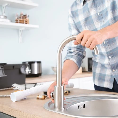 A plumbing professional installing a modern brushed nickel gooseneck faucet onto a new kitchen countertop sink setup.