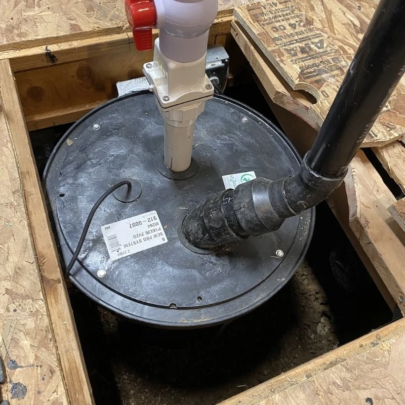 Brand new sewage package ejector pump system installed under a basement subfloor, featuring a heavy-duty red shutoff valve and black PVC discharge line in Niles.