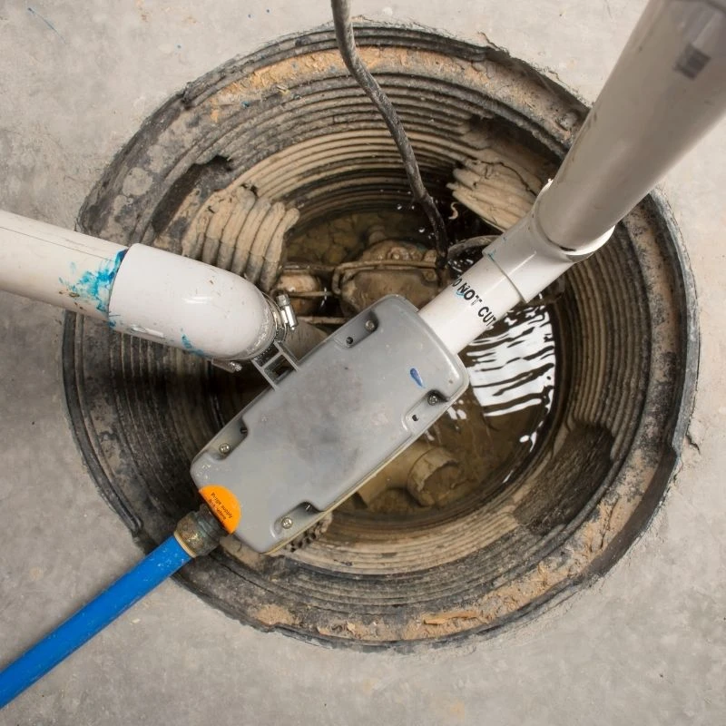Close-up of a newly installed sump pump system featuring a heavy-duty check valve and secure PVC discharge pipes in a Northwest Chicago basement.