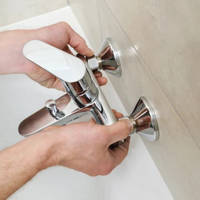 Close-up of a plumbing technician installing a modern polished chrome single-handle faucet onto a bathroom bathtub wall mount.