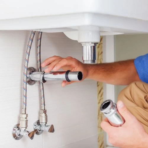 Close-up of a technician replacing the under-sink drainage piping and braided metal supply lines for a bathroom vanity remodel.