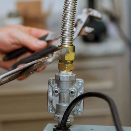 Close-up of a technician using pliers to secure a flexible corrugated stainless steel gas line connector to a fuel appliance valve.