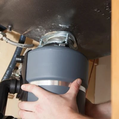 Close-up of hands aligning, lifting, and locking a grey heavy-duty garbage disposal unit onto the under-sink mounting assembly.