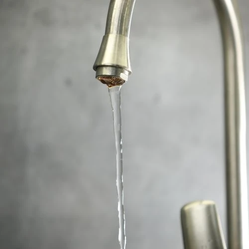 Close-up of low water pressure flow running from a brushed nickel kitchen faucet spout with a clogged aerator.
