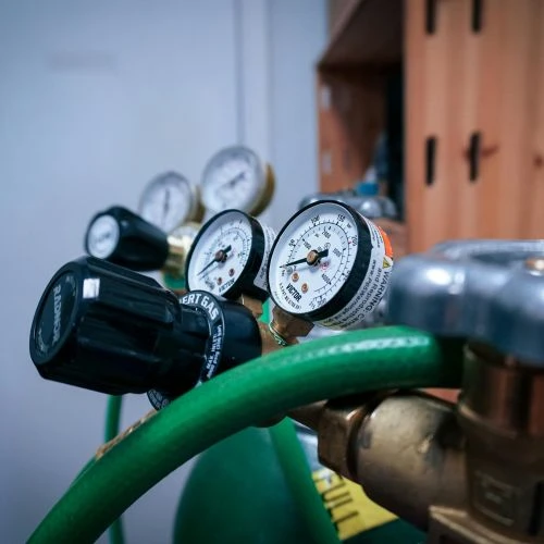 Close-up of pressure gauges and a regulator valve connected to a green storage tank system during a professional gas line test.