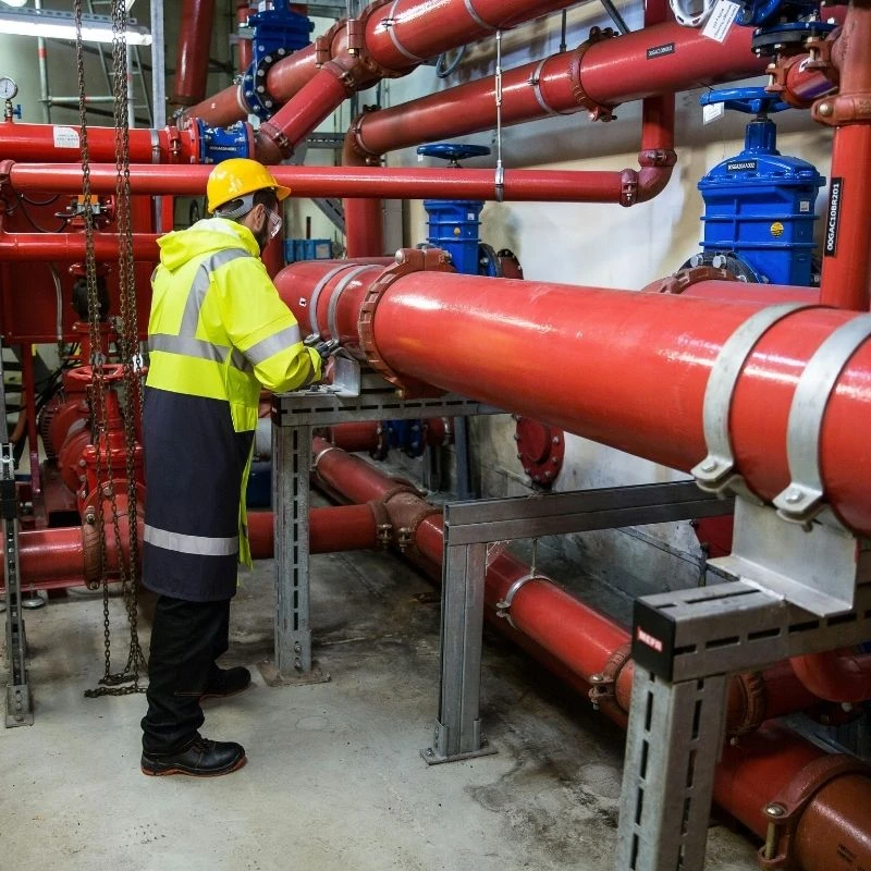 Commercial plumbing contractor in safety gear inspecting large industrial water pipes and heavy-duty blue valves for a facility in Northwest Chicago.
