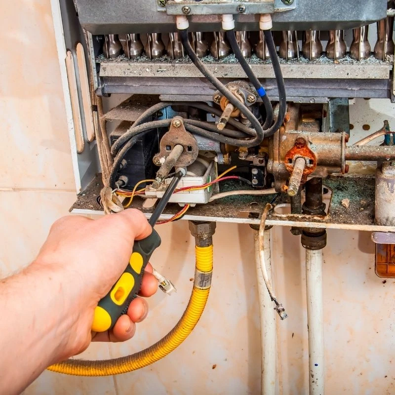 Elevate Plumbing technician carefully repairing the internal burner assembly and gas valve components of a tankless water heater during a service call in Niles.