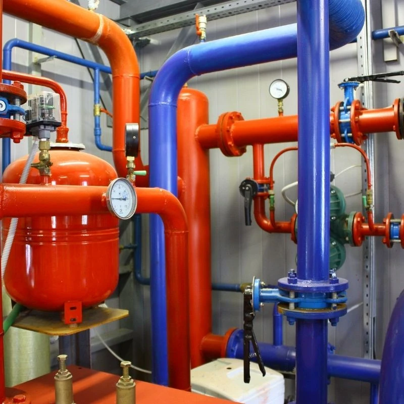 Industrial boiler room showcasing commercial plumbing pipes, pressure gauges, and a high-capacity red expansion tank serviced by Elevate Plumbing.