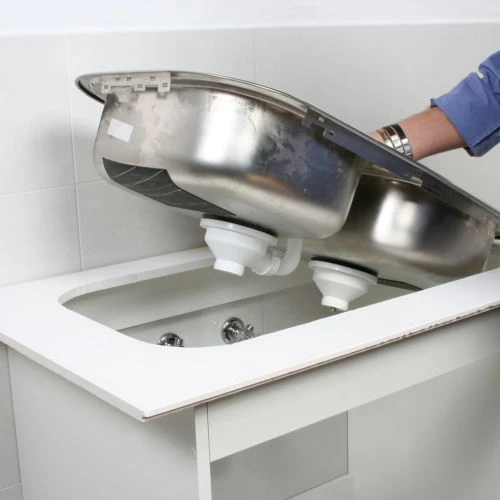 Installer lifting and positioning a double-bowl stainless steel kitchen sink into a newly cut countertop opening.
