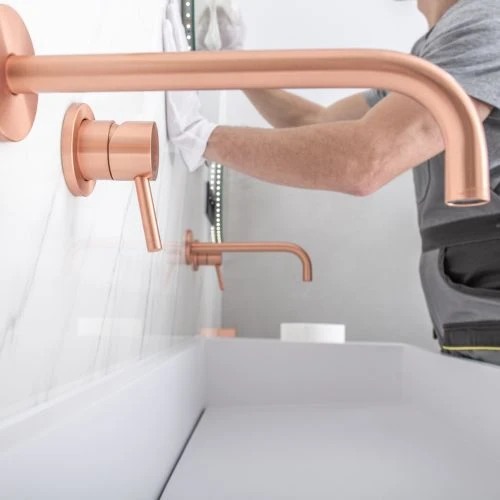 Installing upscale modern rose gold wall-mounted faucets over a clean white bathroom washbasin vanity.