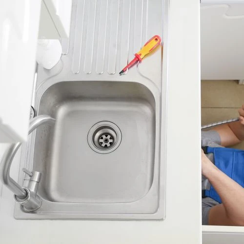 Overhead view of a stainless steel kitchen sink with a screwdriver left on the drainboard during an installation project.