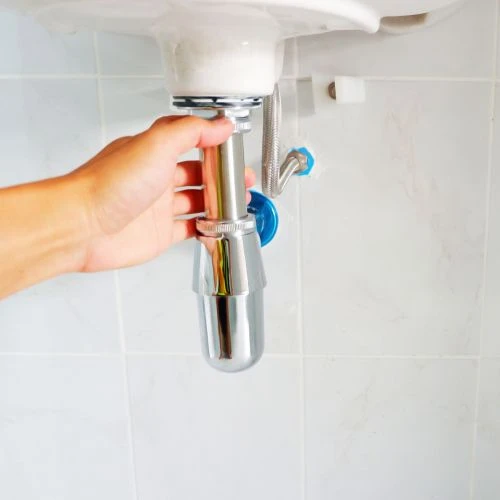 Plumbing technician installing a new chrome bottle trap and drain pipeline extension assembly underneath a bathroom sink.