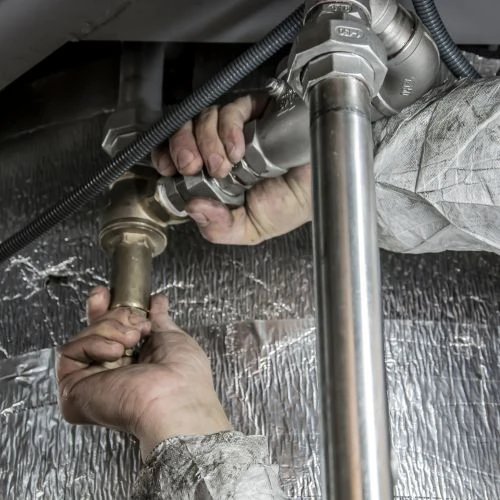Residential plumber connecting metal water supply pipes and brass fittings in a home basement or crawlspace.