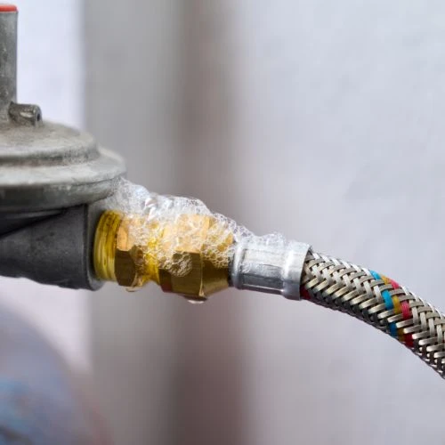 Soap bubble leak test being performed on a brass gas line fitting to identify and locate a hazardous fuel connection leak.