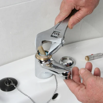 Technician using an adjustable wrench to dismantle and replace internal cartridge components during a bathroom sink faucet repair.
