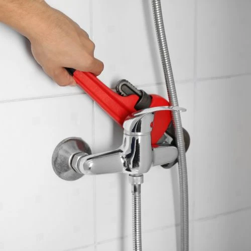 Using a red pipe wrench to tightly secure a modern chrome shower mixer valve fixture to the bathroom tile wall.